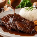 Plato de asado negro venezolano cortado en rodajas y bañado en salsa oscura de papelón, servido en una sartén de hierro