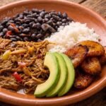 Pabellón criollo venezolano: carne mechada, caraotas negras, arroz blanco y tajadas de plátano maduro en un plato de barro