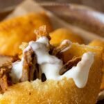 Empanadas venezolanas fritas y doradas, una abierta mostrando el relleno de carne mechada con un chorro de nata, y otras enteras en un bowl de madera