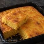 Pan de maíz venezolano dorado en una sartén de hierro, con un trozo levantado que muestra la miga amarilla, húmeda y esponjosa por dentro