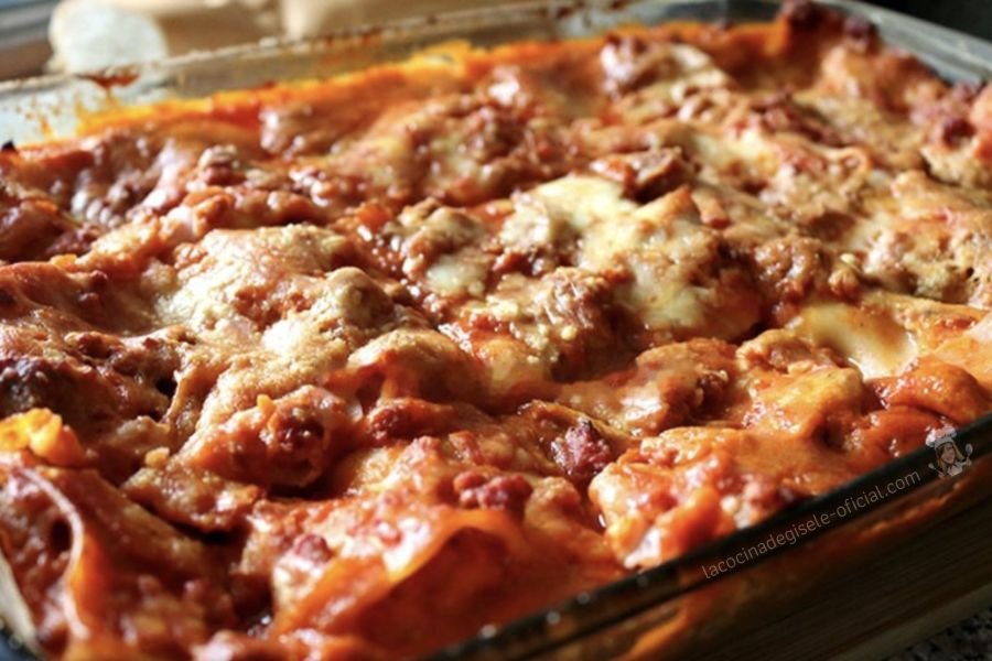 Pasticho venezolano tradicional recién horneado y gratinado con queso en una bandeja de vidrio, con capas de pasta, salsa de carne y salsa blanca